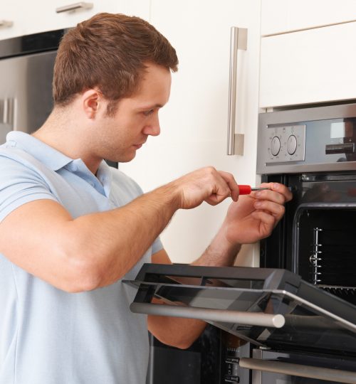 Man Repairing Domestic Oven In Kitchen