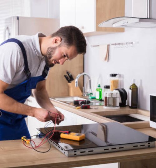 Male Technician Repairing Induction Stove With Digital Multimeter In Kitchen